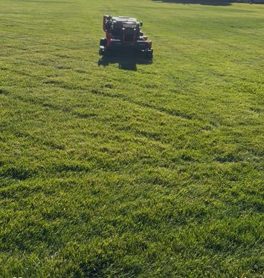A robotic lawn mower cutting grass on a large field in the daylight.