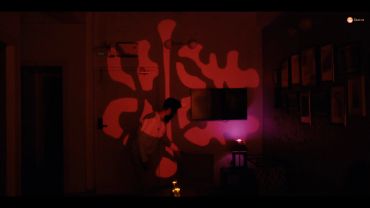 Man in a dark room with red abstract light patterns on the wall.