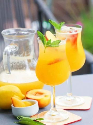 Two glasses of peach cocktail garnished with mint and peach slices.