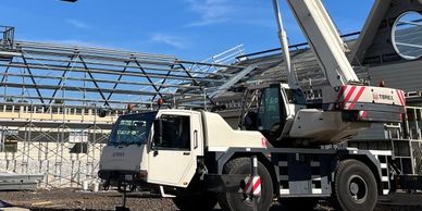 A mobile crane lifting a metal frame structure under a clear blue sky.