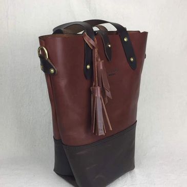 Leather tote with brown upper and dark brown bottom. Brown hand straps with brass saddle rivets.