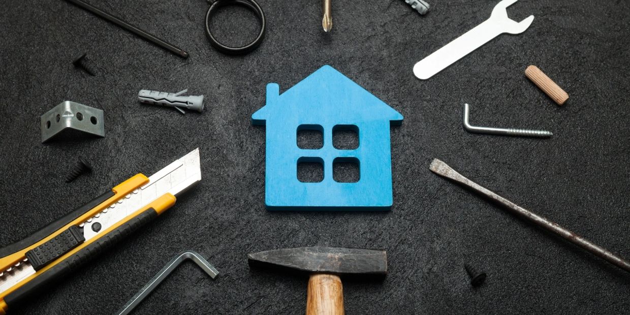 Various construction tools placed around a blue house cutout on a dark background, symbolizing home improvement, repairs, and building services.