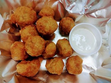 Fried hush puppies served with a side of creamy dipping sauce on foil.