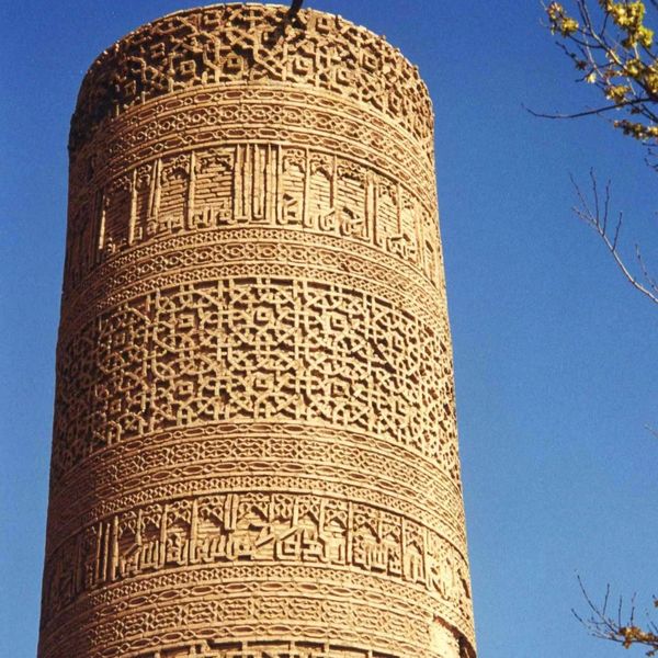Intricate ancient tower with detailed geometric and calligraphic carvings against a clear blue sky.