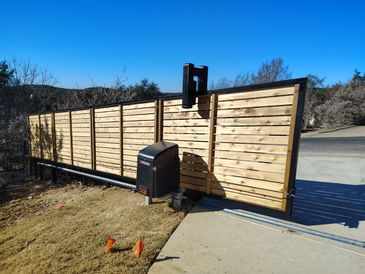 Automated wooden driveway gate with security camera on a sunny day.