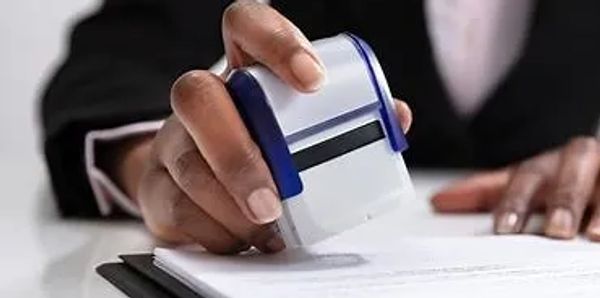 A person stamping a document with a blue and white stamp.