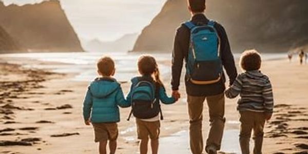 A man and three children walk along a sandy beach at sunset.