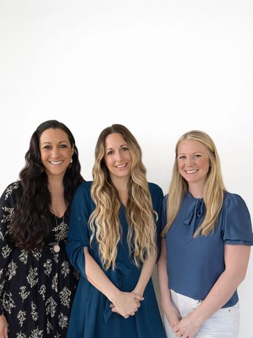 Three smiling women with long hair posing against a white background.