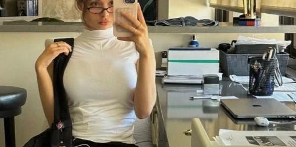 Woman taking a mirror selfie in a white top and glasses.