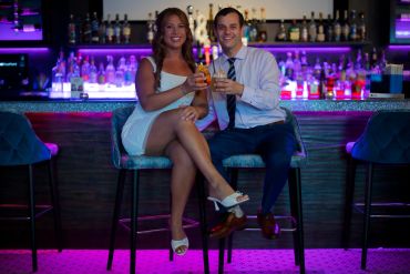 Couple drinking cocktails at a bar, smiling and toasting.