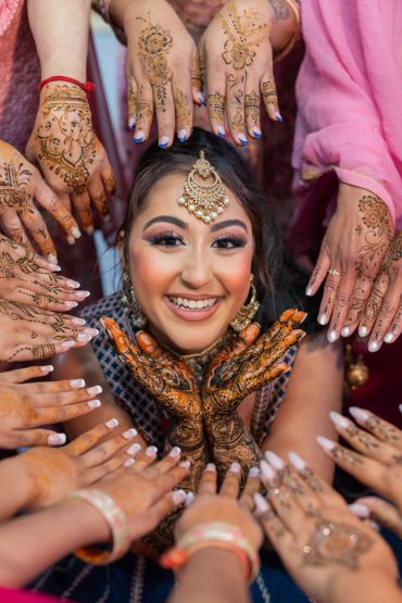Smiling woman with henna-decorated hands surrounded by similarly adorned hands.