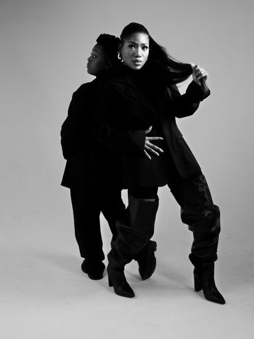 Black and white portrait of two people standing back to back in stylish outfits.