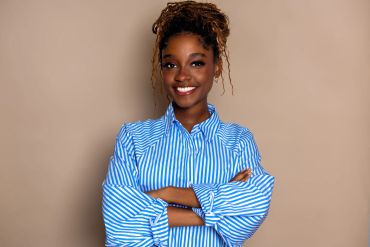Confident woman in blue-striped shirt smiling, arms crossed.
