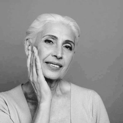 Elegant elderly woman with white hair gently touching her face in a serene black and white portrait.