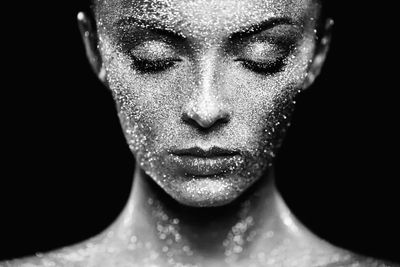 Close-up of a face covered in glitter with eyes closed against a black background.