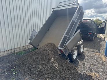 A trailer unloading gravel beside a black utility vehicle.