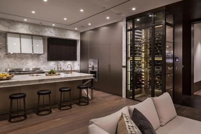 Modern kitchen with marble countertops, dark cabinetry, and a glass-enclosed wine rack.