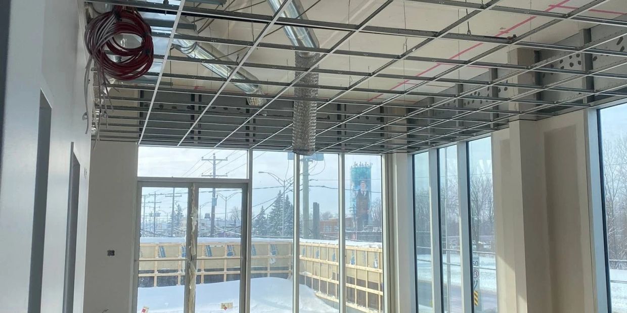 Intérieur en construction avec plafond ouvert et grande baie vitrée.