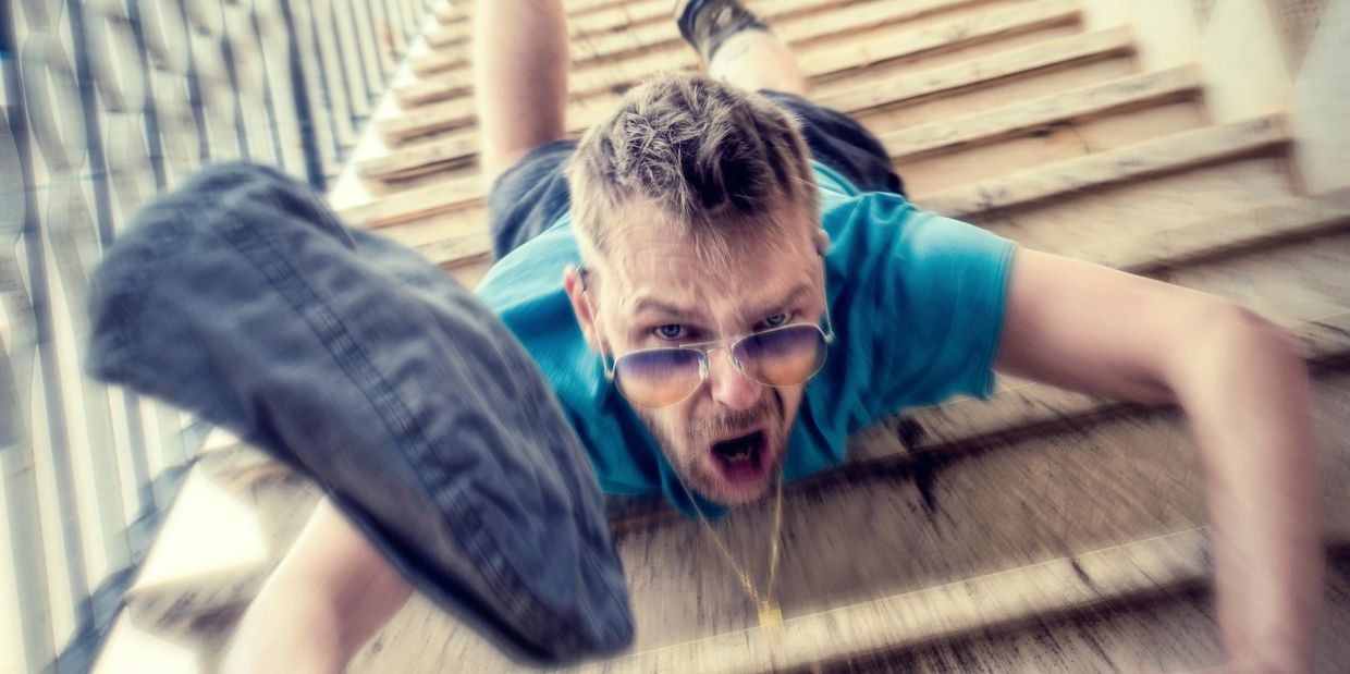 Man falling down stairs with a shocked expression, shoe flying off.