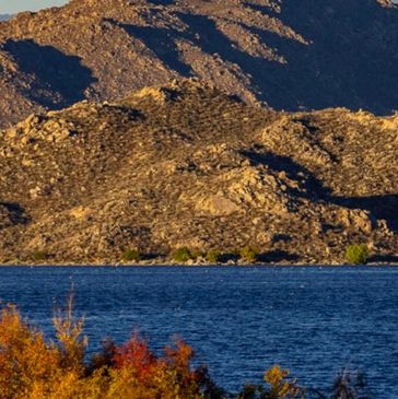 A serene lake with autumn trees and rocky hills in the background.