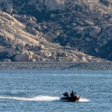 A person on a small boat speeding across a lake with rocky hills in the background.