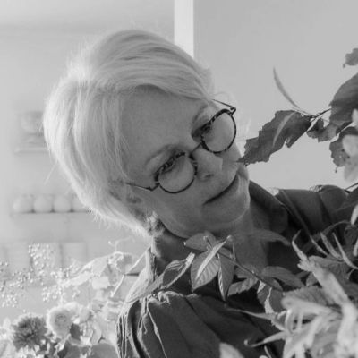 Elderly woman with glasses arranging autumn leaves indoors.