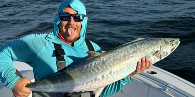 Man holding a large fish on a boat, smiling with tongue out.
