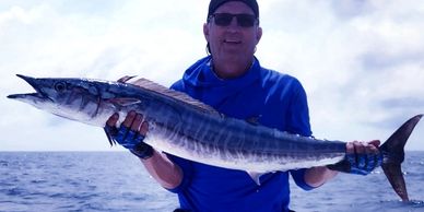 Man holding a large fish on a boat under a cloudy sky.