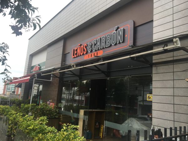 Entrance of Leños & Carbón restaurant with outdoor greenery.