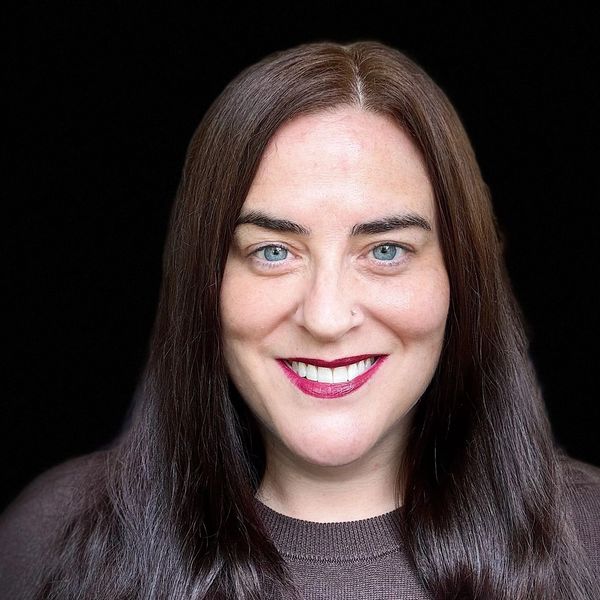 Smiling woman with long brown hair against black background.
