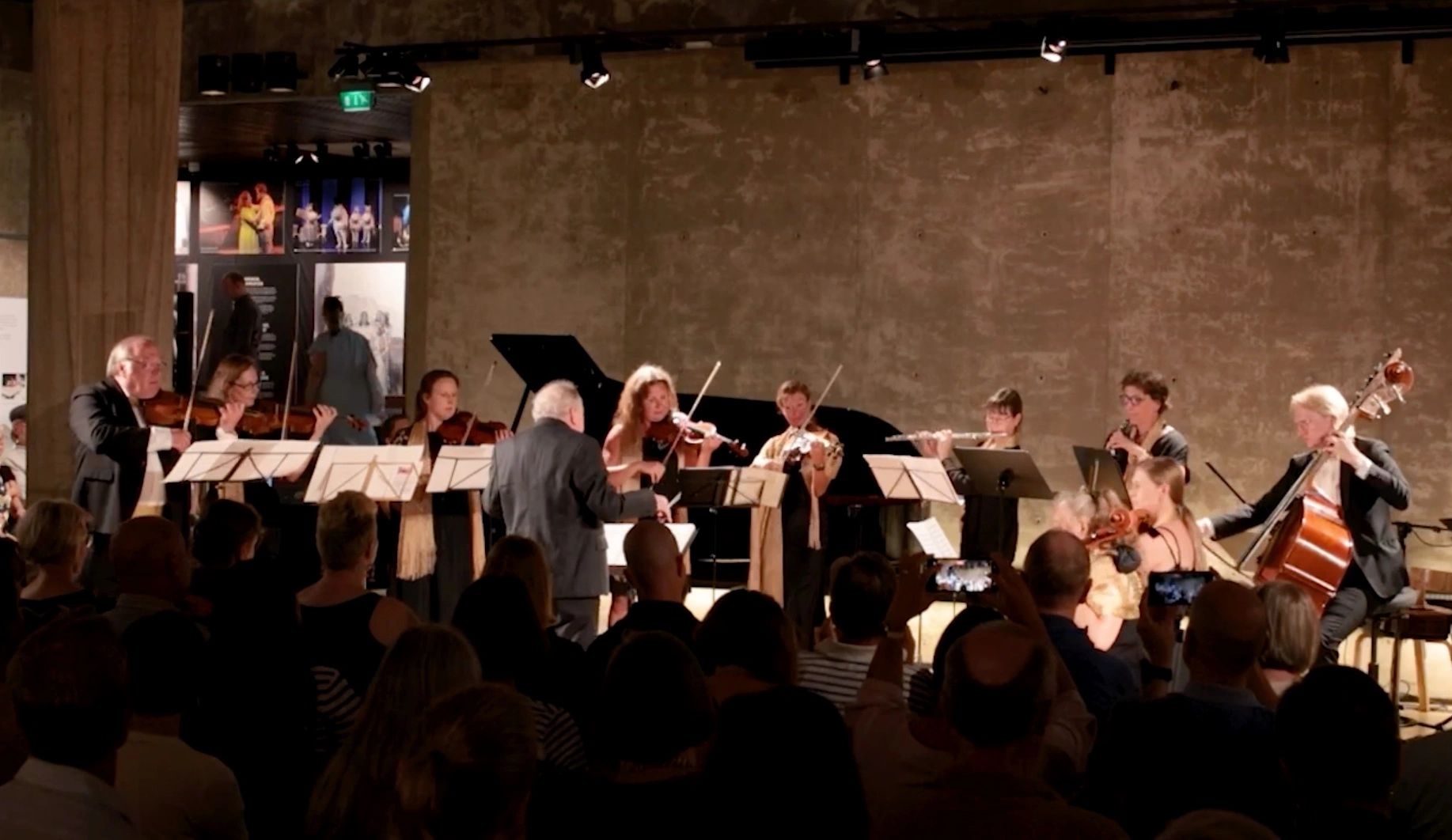 Chamber orchestra performing in an intimate concert hall with attentive audience.