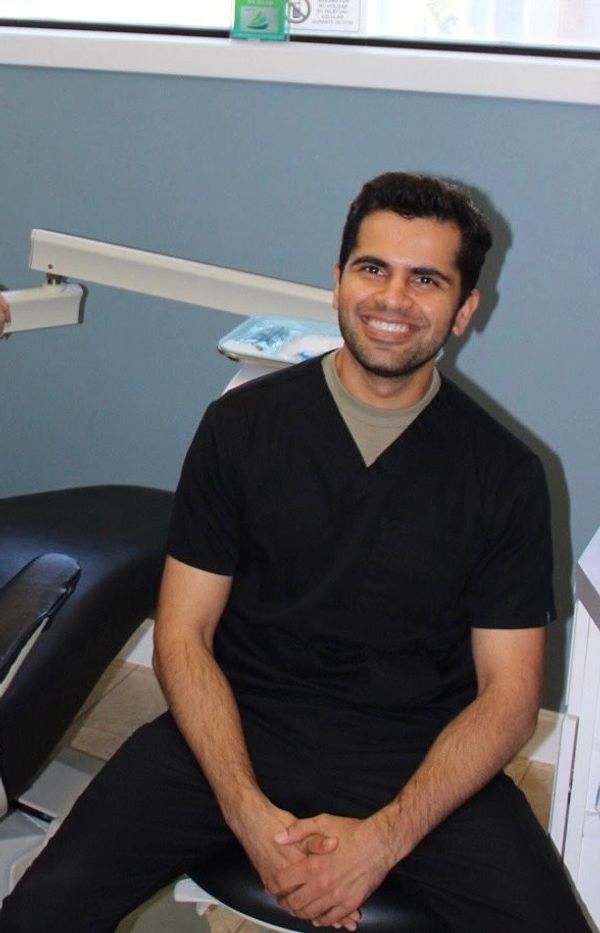 A man in black scrubs smiling while seated in a clinical setting.