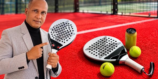 Man showcasing a padel racket on a red court with tennis balls.