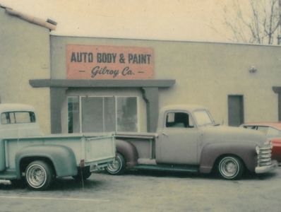 Vintage auto body and paint shop with classic trucks parked outside.