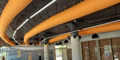Modern office ceiling with orange ducts and linear lights.