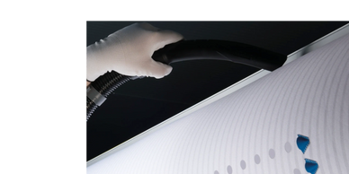 Hand holding a vacuum hose near a white surface with blue accents.