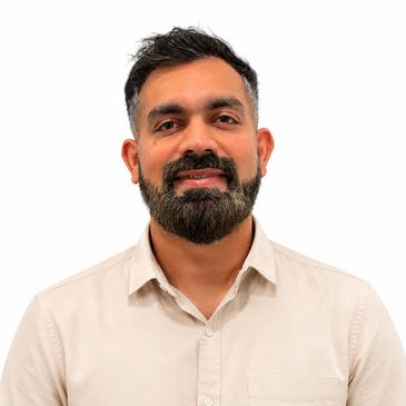 Smiling man with beard and short hair in a beige shirt.