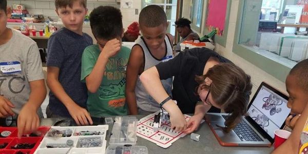 Children engaged in a robotics activity with a laptop and parts.