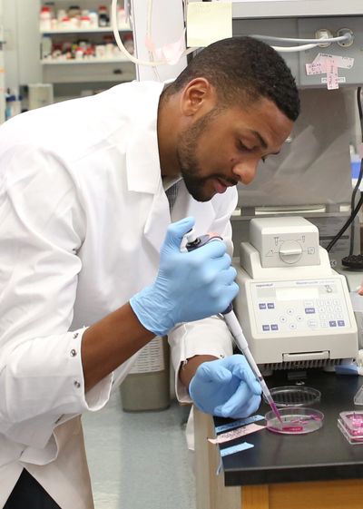 Photo of a scientist in a lab coat with a pipette and petri dish.