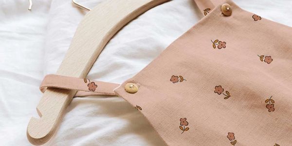 A baby romper with a delicate floral print, on a wooden hanger, placed on a soft white fabric.