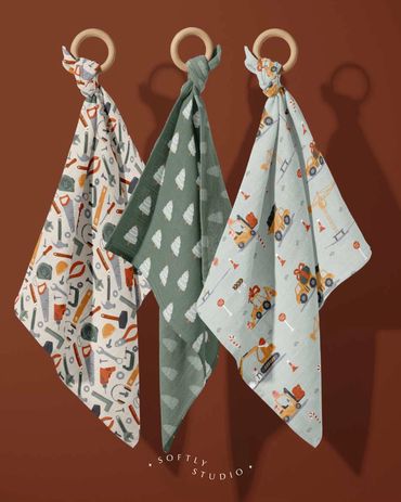 Three muslin cloths with construction, tools and Christmas tree prints, hung on wooden rings.