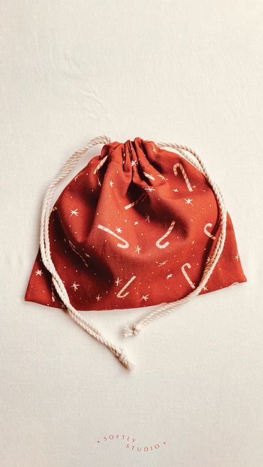 A red drawstring gift bag featuring candy canes and stars on a festive holiday print.