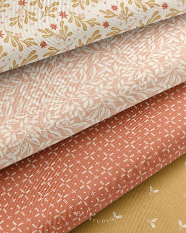 Folded fabrics with soft leaf patterns, geometric designs, and delicate holiday accents.