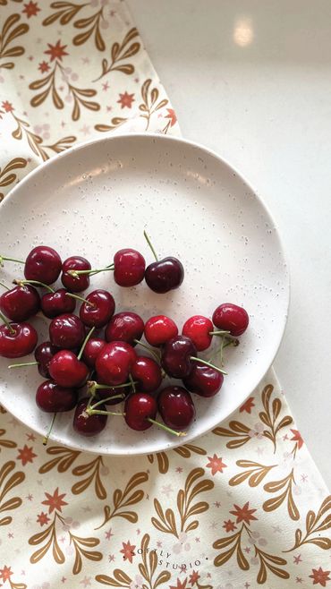 A festive tea towel with a leaf and star pattern, topped with a plate of fresh cherries.