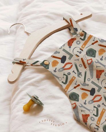 Baby overalls in construction-themed fabric with tools and equipment, paired with a pacifier.