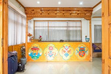 Reception desk with traditional artwork and tip box in a cozy lobby.