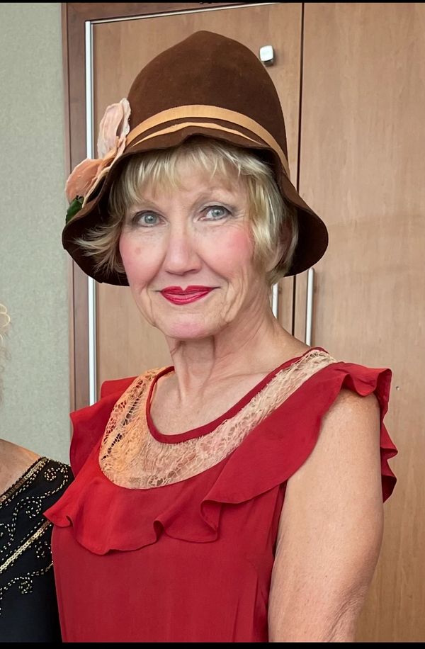 Smiling woman in a red dress and brown hat.