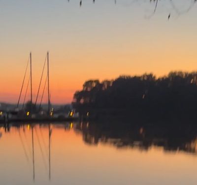 Sailboats docked at sunset with reflections on calm water.