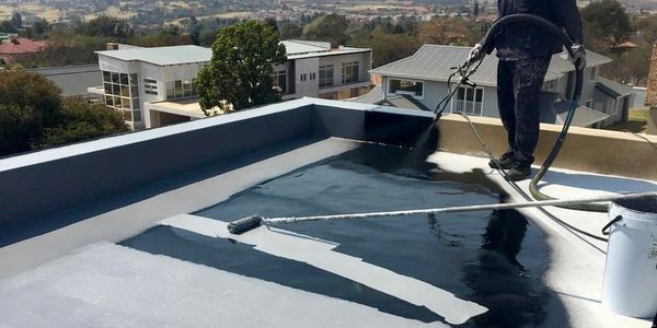 Person applying black waterproof coating on roof.