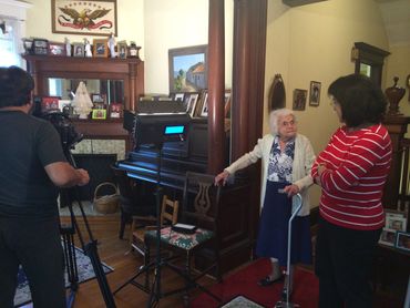 Elderly woman being interviewed at home with camera and lighting setup.